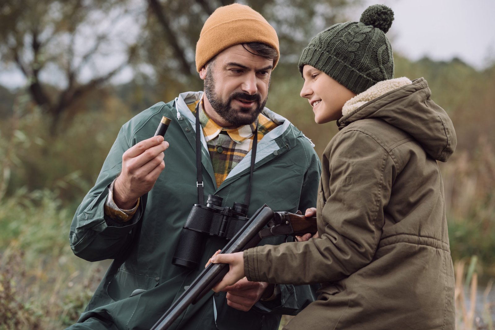 Father showing son how to load bullet in gun for hunt